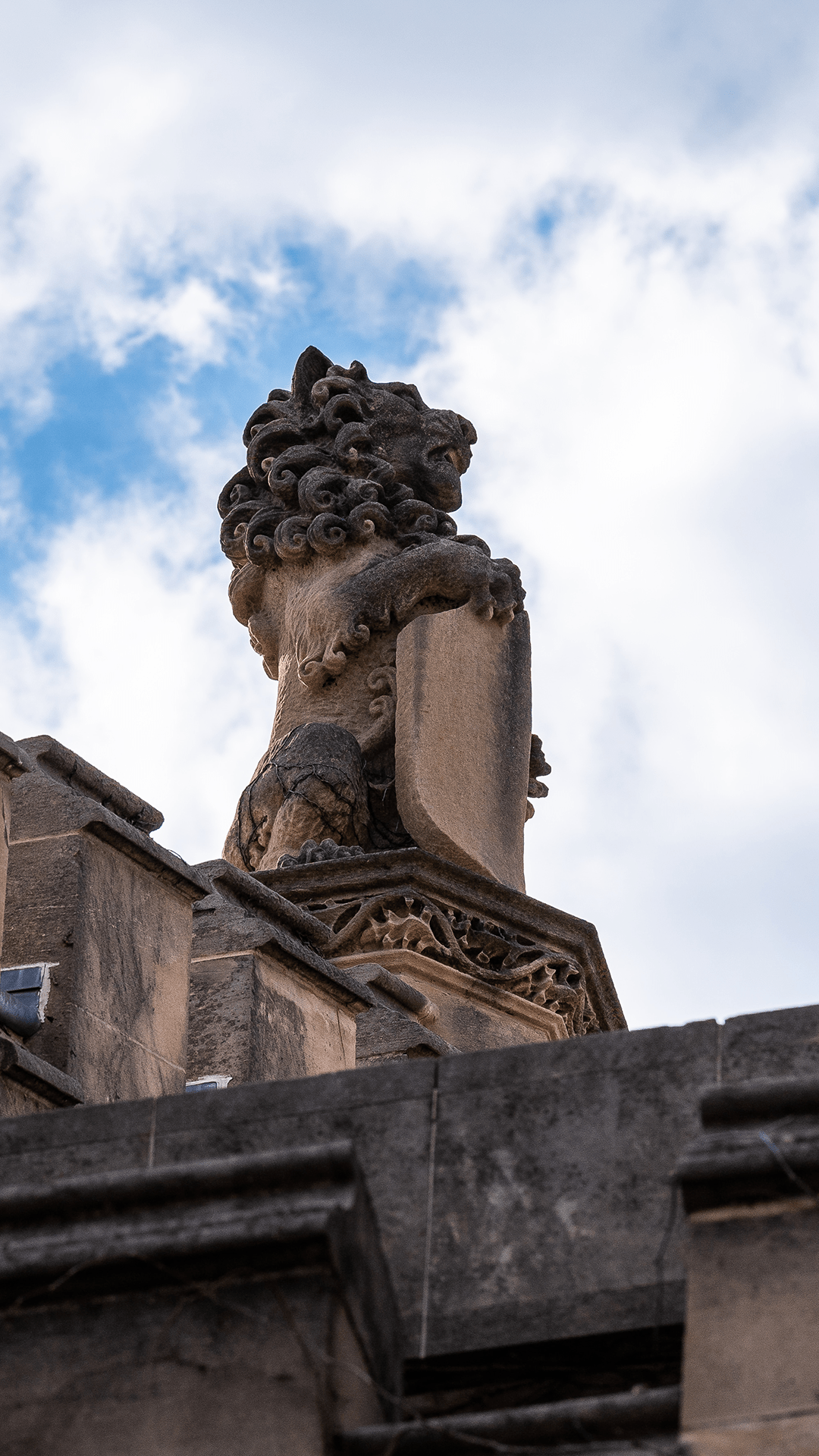 Stone lion carving atop a building against a blue sky with clouds